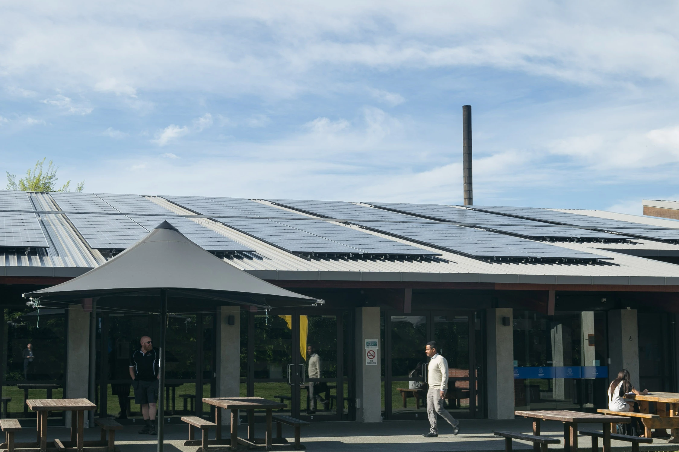Cafe that is closed with solar panels installed on roof, people and seating arranged outside on path