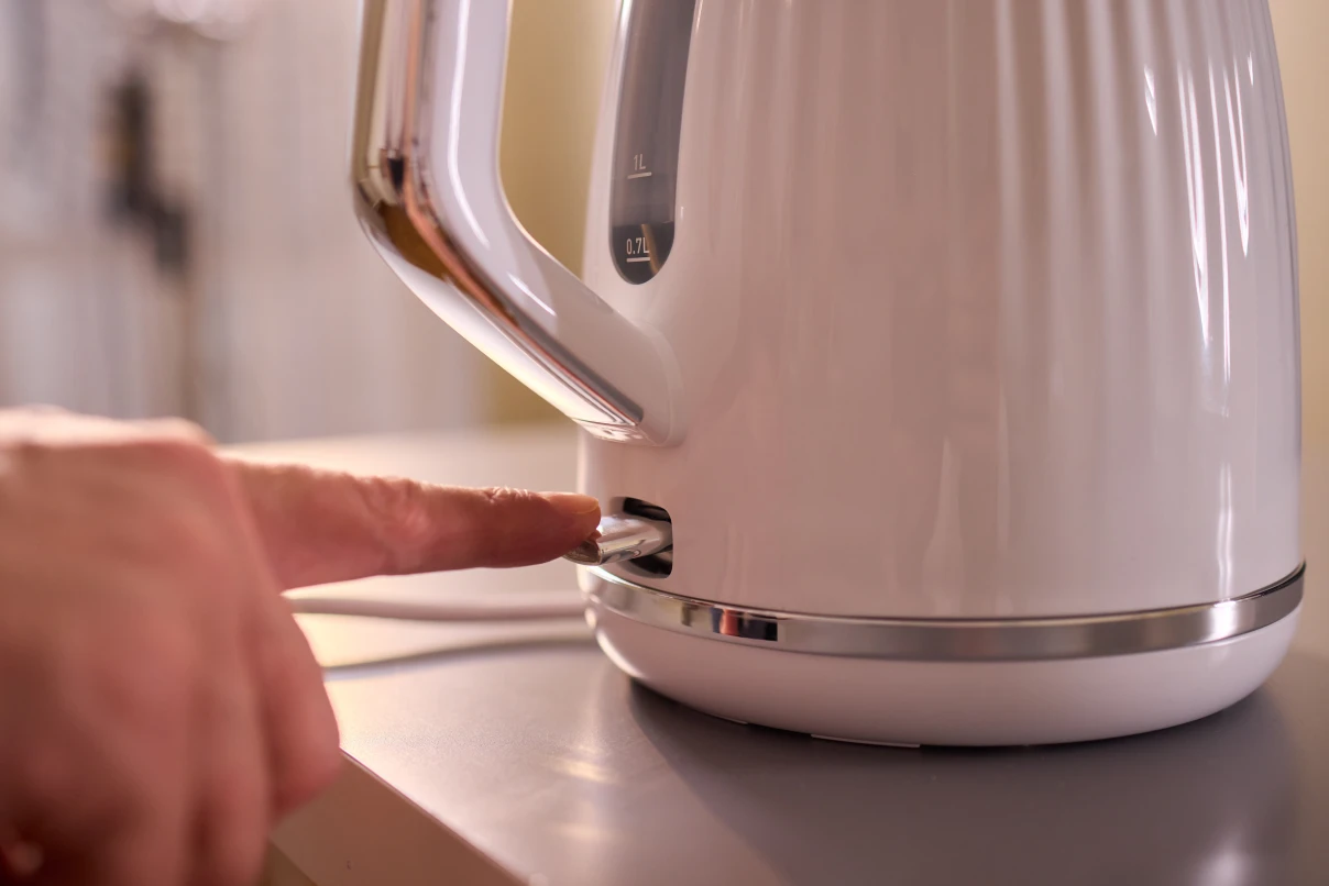 Kettle on bench, hand pushing switch to start boiling