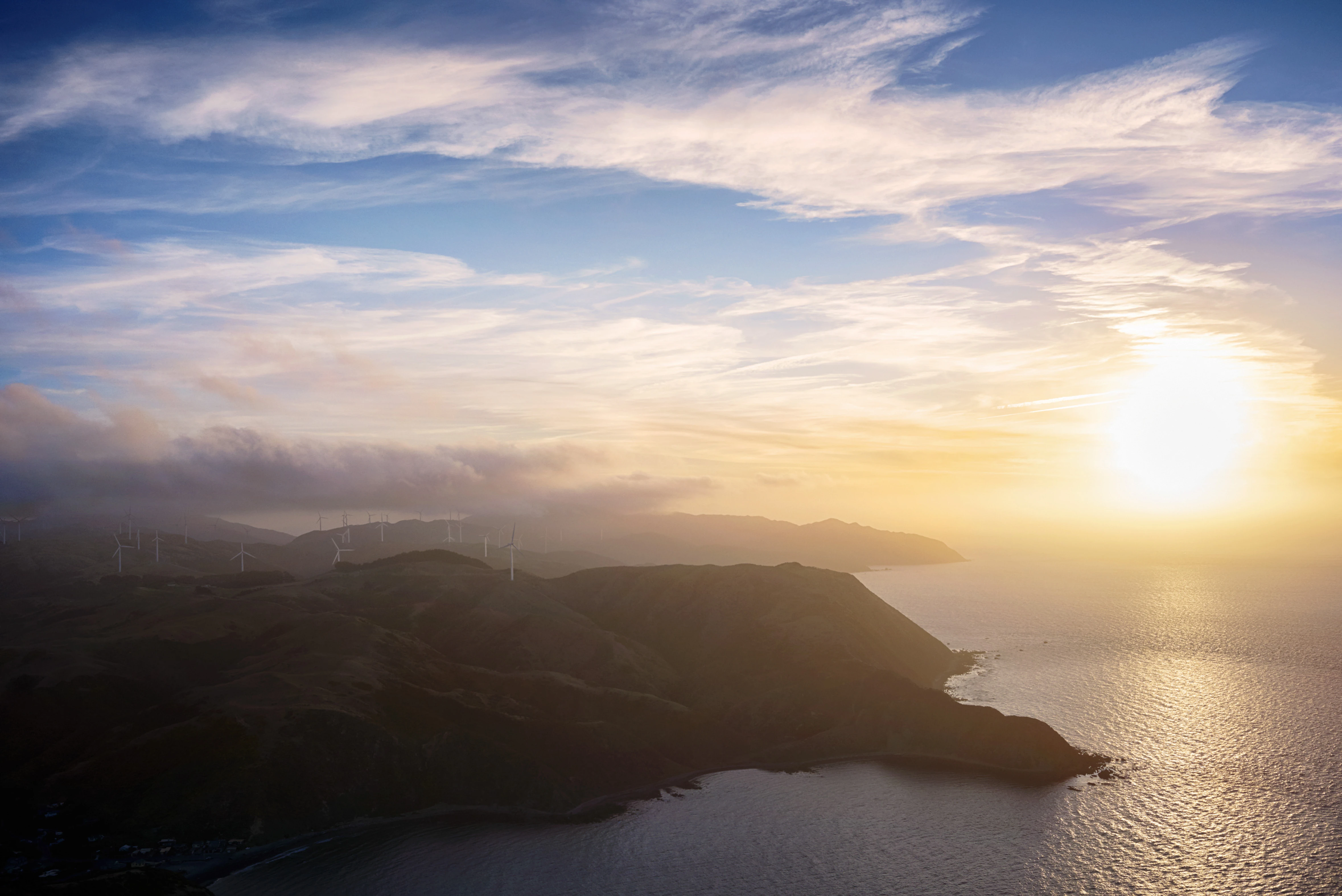 Ariel shot of New Zealand hills and ocean with wind turbines scattered in the land.