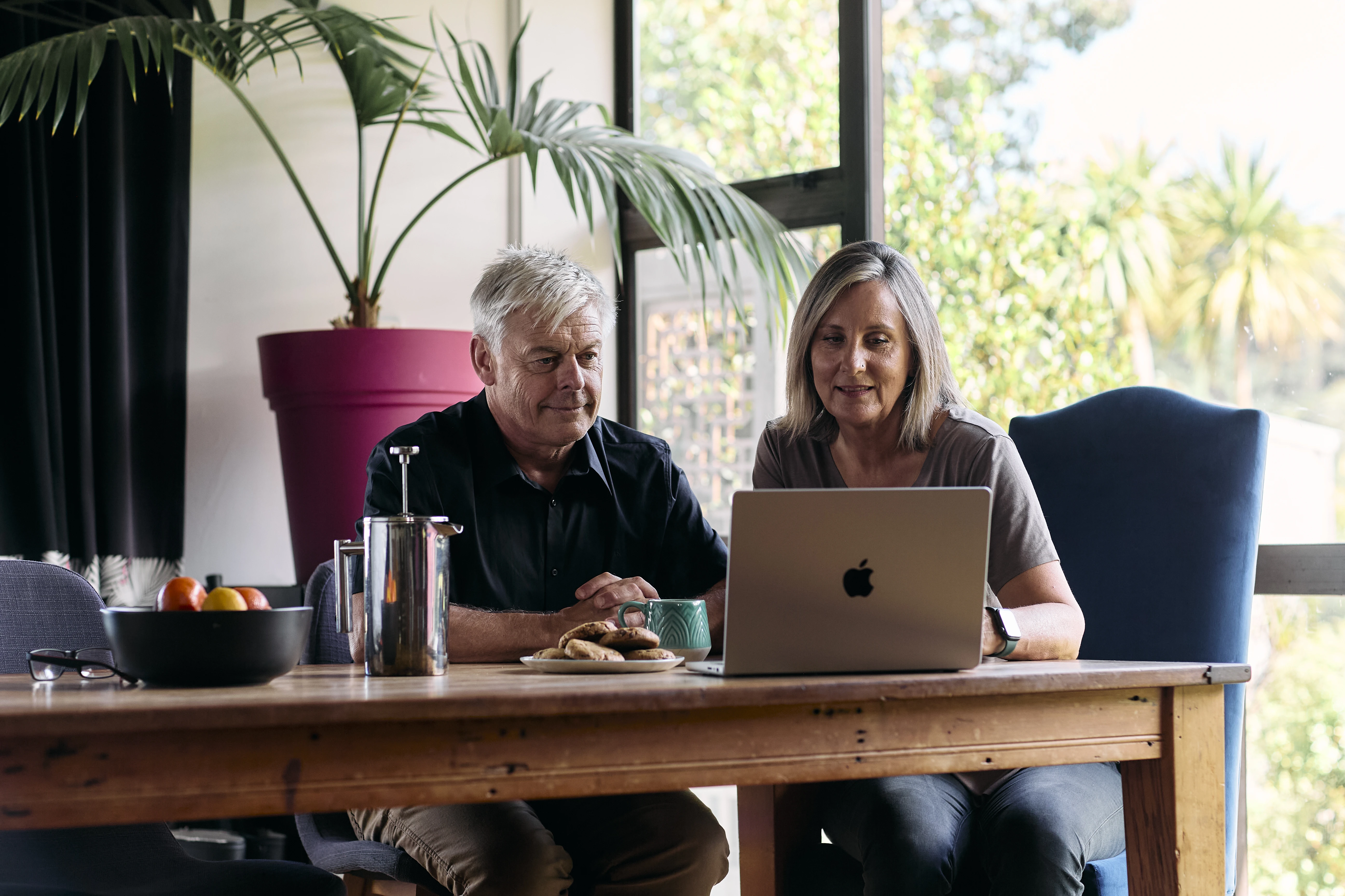 Home assessment, a man and woman sit at a dining table looking at a laptop together.
