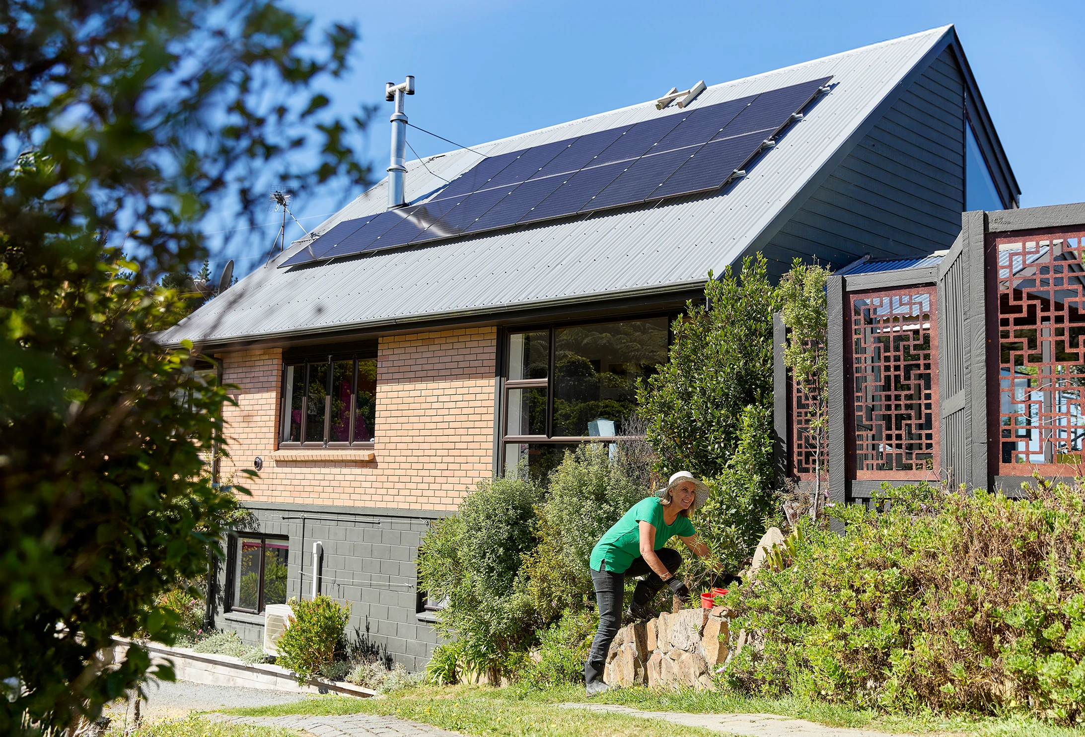 Residential house with solar panels on roof and a woman gardening.