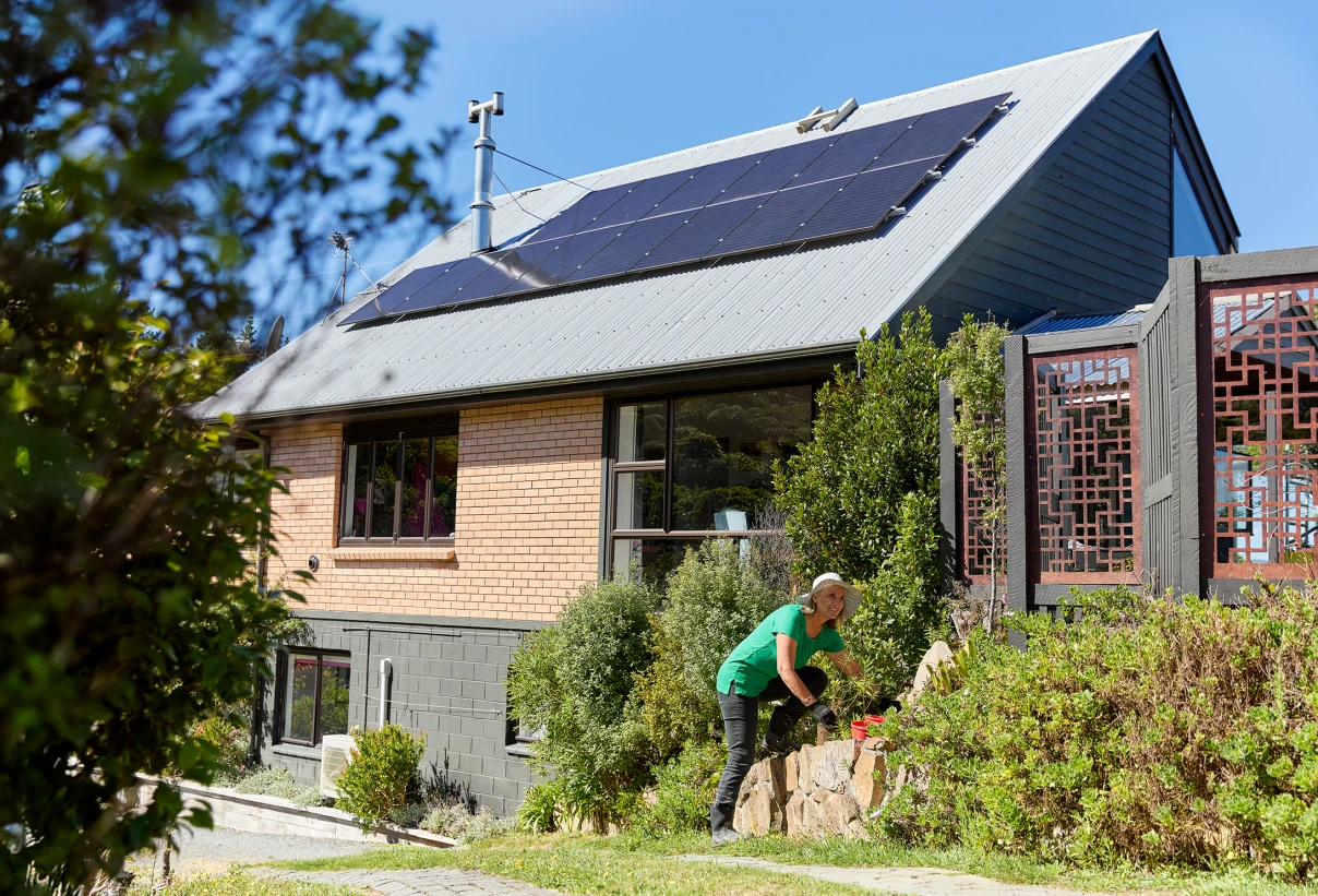 Residential house with solar panels on roof and a woman gardening.