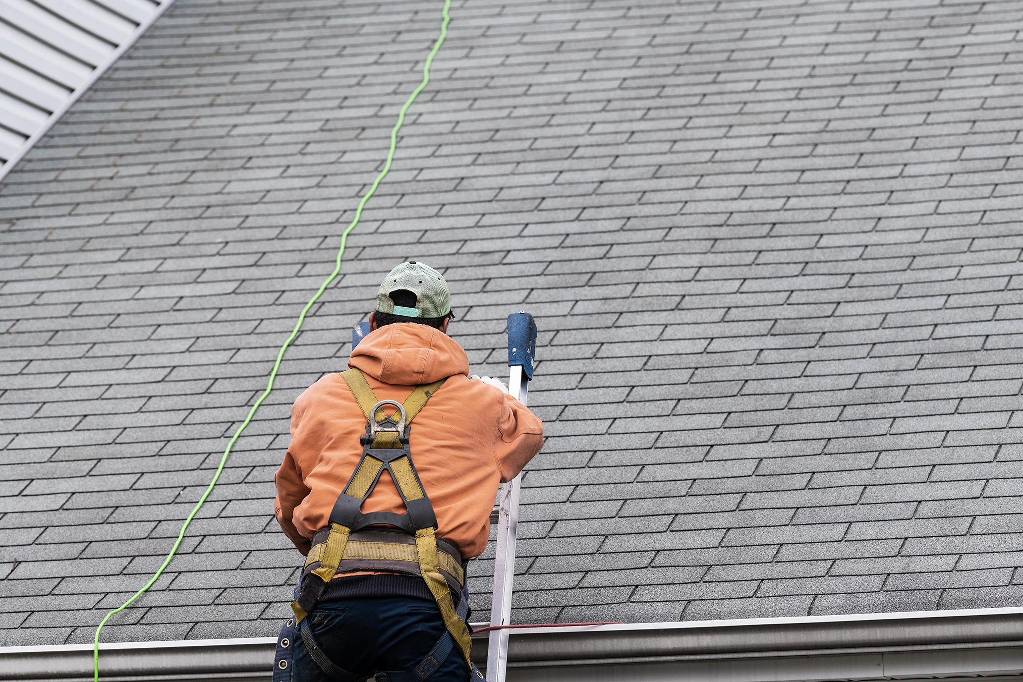 A man in a safety harness is climbing a ladder up to a roof.