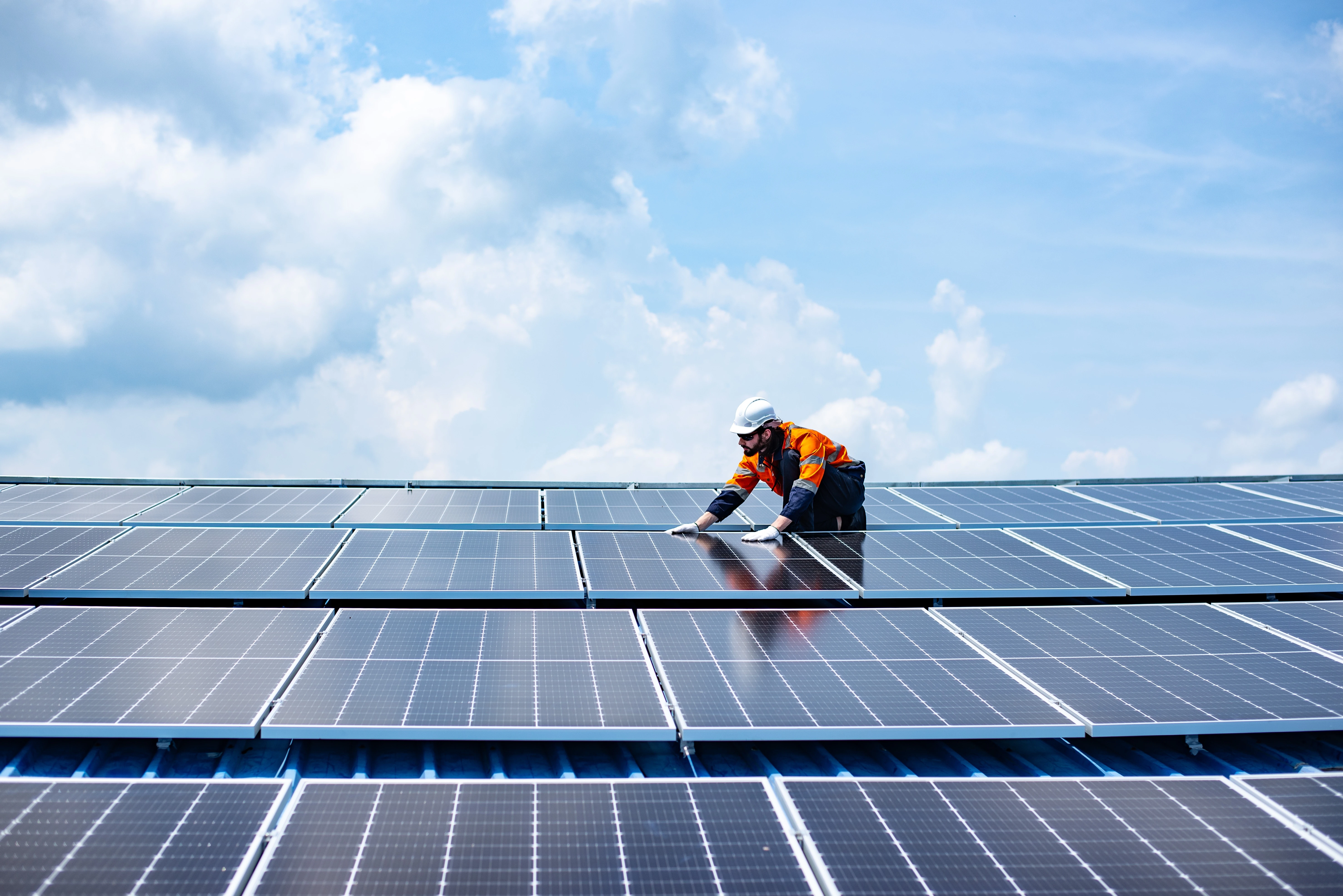 A worker wearing hi-vis is installing solar panels on a large roof.
