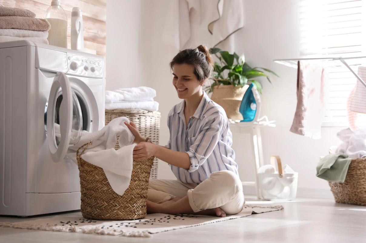 Young woman taking laundry out of washing machine at home