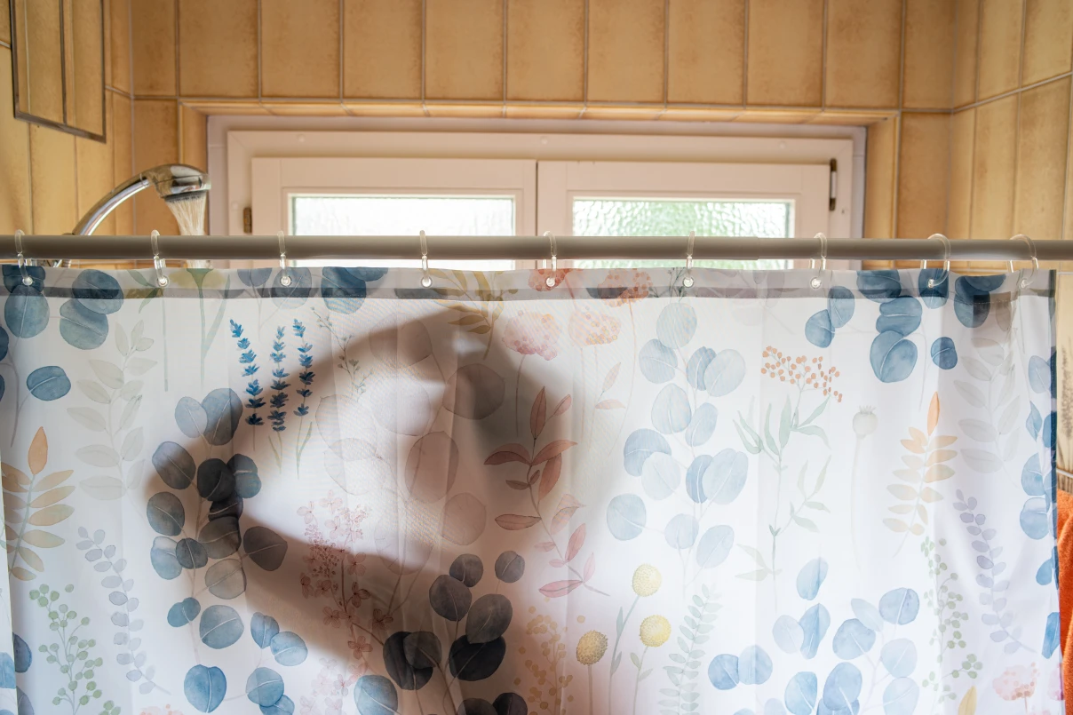 Man in shower silhouetted partially through curtain